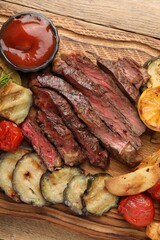 Delicious grilled beef with vegetables and tomato sauce on wooden table, top view