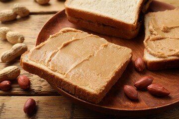 Tasty peanut butter sandwiches and peanuts on wooden table, closeup