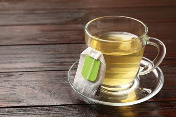 Tea bag and glass cup of hot beverage on wooden table, space for text