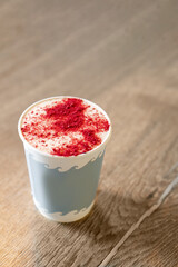 Coffee drink with foam and freeze-dried raspberries in a paper glass in a cafe