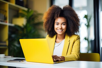 Young happy afro american woman in yellow jacket working on laptop