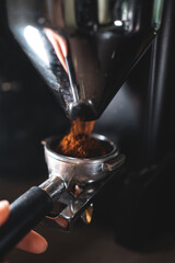 barista with holder grinding coffee beans with professional grinder machine