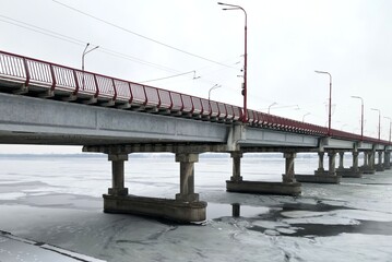 Road bridge on winter river. Large concrete bridge with red railings and lamp posts, river is covered with ice.