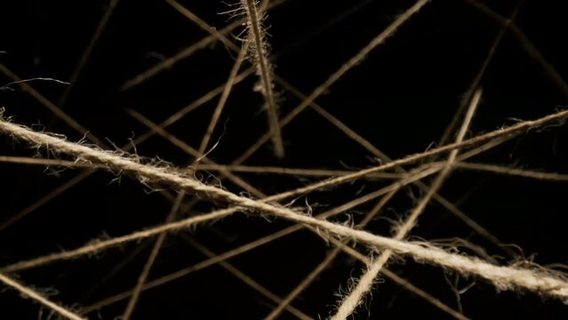 Macro dolly shot camera flies through sisal ropes, threads plexus lighted with spot light on black background, twine lines in dark, abstract chaotic interweaving, background for titles or logo