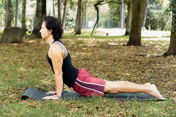 a man practicing yoga in the middle of the park, practicing bhujangasana pose
