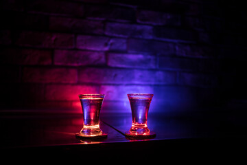 Cold vodka glass on a dark background in the neon light or glasses of russian vodka on bar...