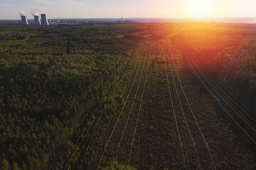 Smoking cooling towers at nuclear power plant and powerlines in forest. Sunset time.  Aerial view