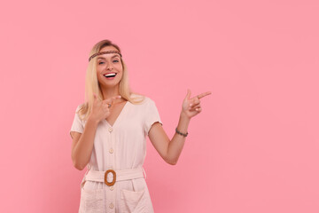 Portrait of happy hippie woman pointing at something on pink background. Space for text