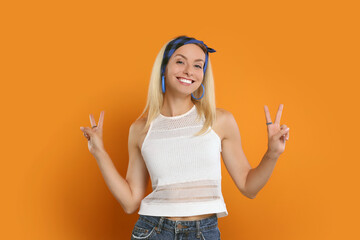 Smiling hippie woman showing peace signs on orange background