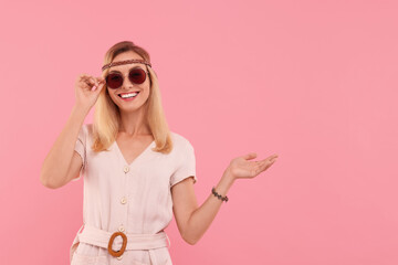 Portrait of smiling hippie woman in sunglasses on pink background. Space for text