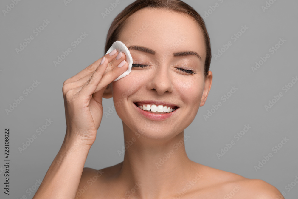 Wall mural smiling woman removing makeup with cotton pad on grey background, closeup