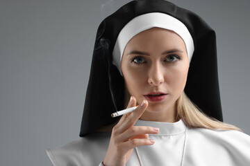 Woman in nun habit smoking cigarette on grey background. Space for text