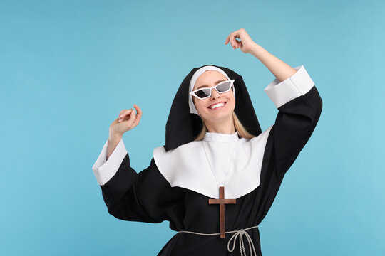 Happy woman in nun habit and sunglasses against light blue background