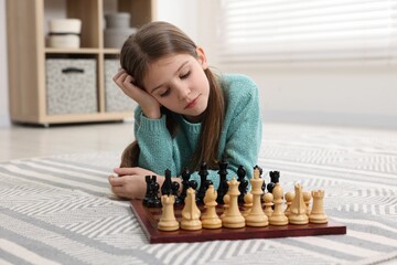 Cute girl playing chess on floor in room