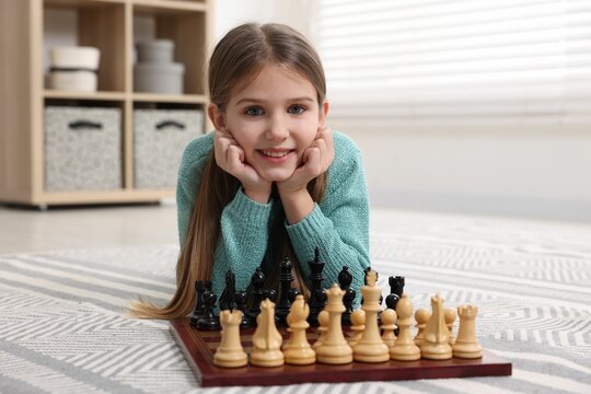 Cute girl playing chess on floor in room