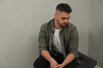 Fototapeta premium Sad man sitting near light grey wall. Space for text