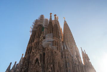 Barcelona's Sagrada Familia, by Gaudi, shines under the sun with spires touching the blue sky. Its...