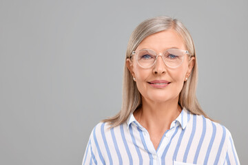 Portrait of beautiful middle aged woman in eyeglasses on light grey background, space for text