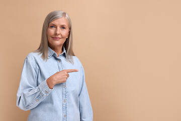 Portrait of beautiful middle aged woman pointing at something on beige background, space for text