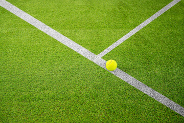 Closeup of one yellow tennis ball or paddle tennis and white lines on green court. Horizontal sport poster, greeting cards, headers, website