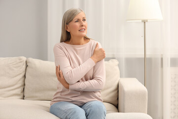 Mature woman suffering from pain in arm on sofa at home. Rheumatism symptom