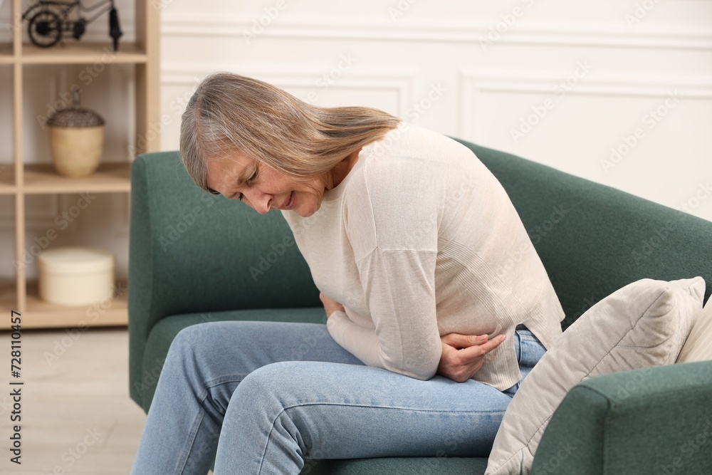 Wall mural Menopause. Woman suffering from abdominal pain on sofa at home