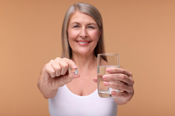 Beautiful woman with vitamin capsule and glass of water on beige background, selective focus