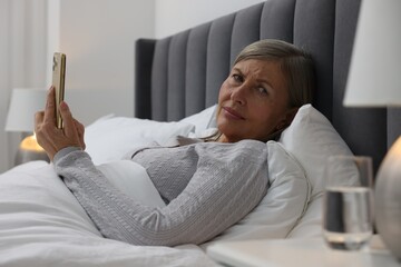 Menopause. Sleepless woman using smartphone in bed indoors