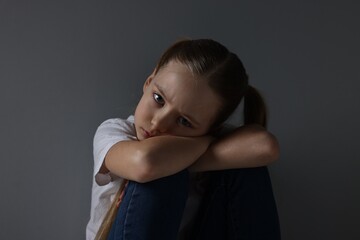 Sad girl sitting near dark grey background