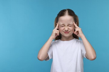 Little girl suffering from headache on light blue background. Space for text