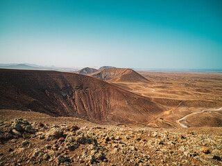 Volcanic desert landscape with mountains and the ocean visible in the background.