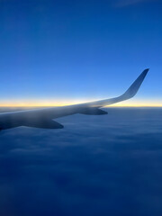 Sunset beyond the horizon seen through the window of a plane flying above the clouds