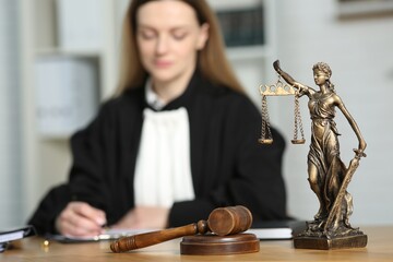 Judge working with document indoors, selective focus. Figure of Lady Justice and mallet on wooden...