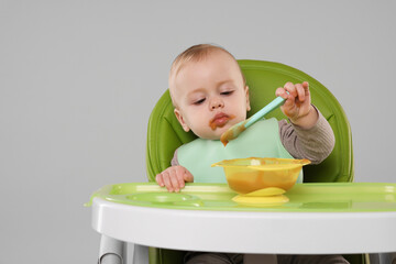 Cute little baby eating healthy food in high chair on gray background, space for text