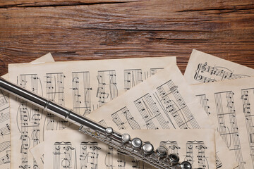 Sheets with musical notes and flute on wooden table, flat lay
