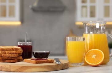 Breakfast served in kitchen. Crunchy toasts, jam and orange fresh on white table