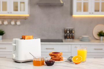 Making toasts for breakfast. Appliance, crunchy bread, honey, jam and orange fresh on white table in kitchen