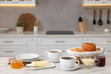 Breakfast served in kitchen. Fresh croissants, coffee, butter, jam, honey and sweetened condensed milk on white table