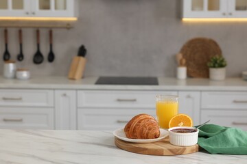 Breakfast served in kitchen. Fresh croissant, jam and orange juice on white table. Space for text