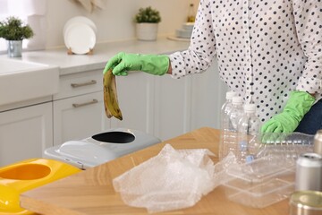 Woman separating garbage at wooden table indoors, closeup