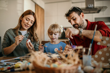Mom, dad, and child immersed in decorating Easter eggs in the cozy dining room