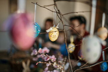Parents and their little one creating beautiful Easter eggs at the dining room table, focus on a...