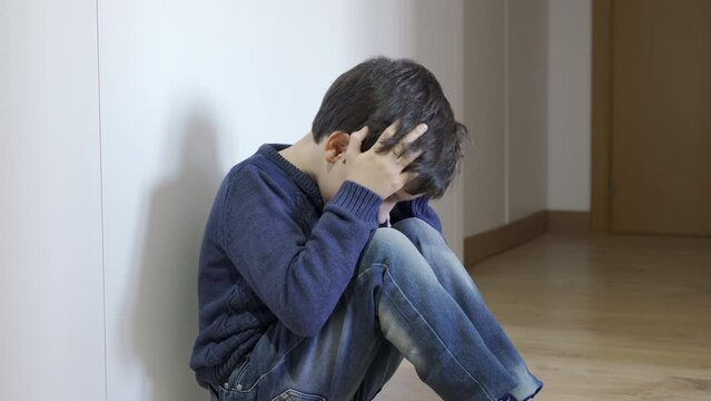 Upset problem child with head in hands sitting on floor concept for bullying, depression stress or frustration at home