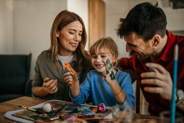 Three-person family enjoying a delightful Easter egg painting session in their dining room