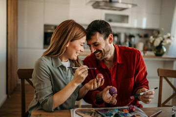 Joyful couple immersed in Easter spirit, delicately decorating vibrant eggs with love