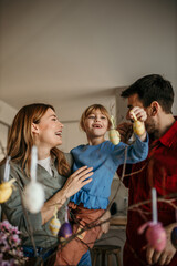 Parents and their child decorating eggs with bright hues, surrounded by the festive atmosphere of their dining room