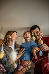 Family of three immersed in the artistic process of painting eggs and embellishing their Easter tree in the dining room