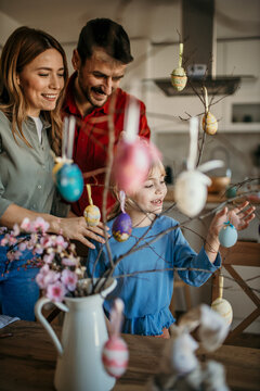 Happy family gathered around the dining table, immersed in painting eggs and beautifying their Easter tree