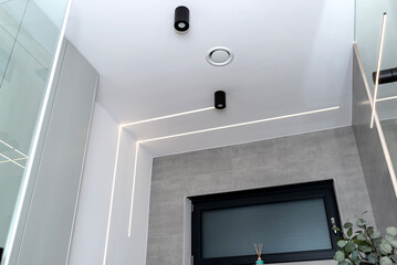 LED light strips mounted in the wall and ceiling in a modern bathroom, visible ventilation...