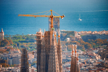 Closeup of Sagrada Familia's spires and construction crane in Barcelona, Spain, with the cityscape...